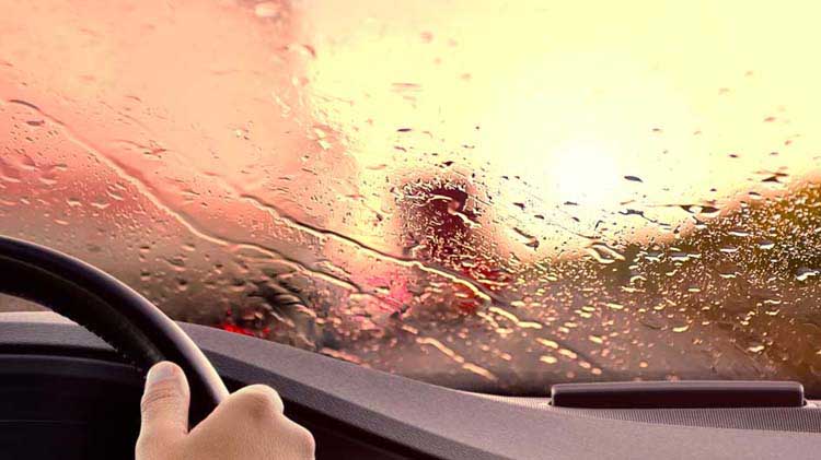 Rain water on windshield and drivers side window of car driving on highway