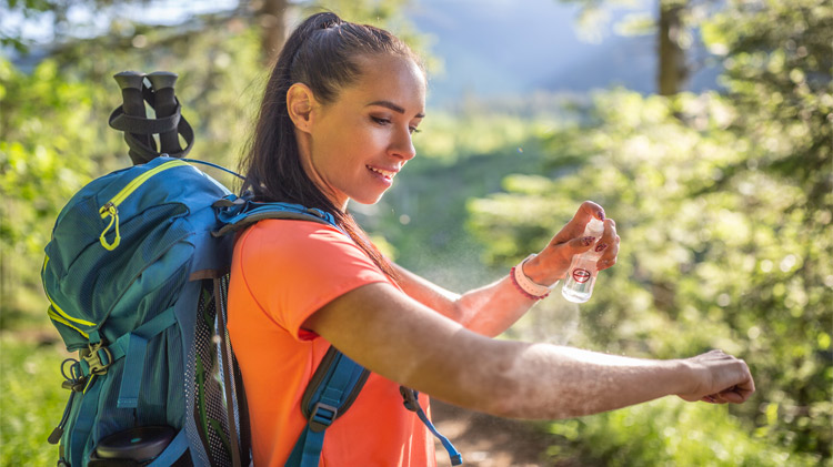 A woman applies bug spray to her hands to prevent bug bites during hike.