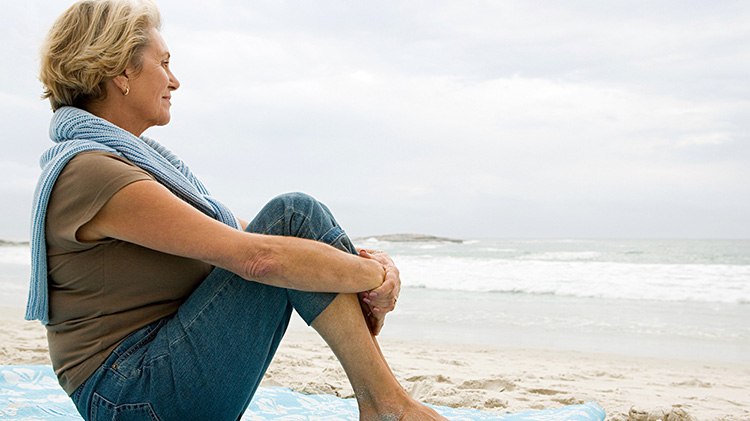 Woman sitting on a blanket at the beach looking out onto the water.