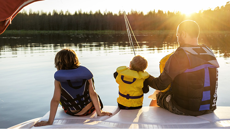 Father and two children fishing off their boat on a sunny lake.