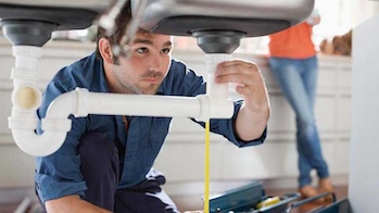 A plumbers works on sink drain under the counter