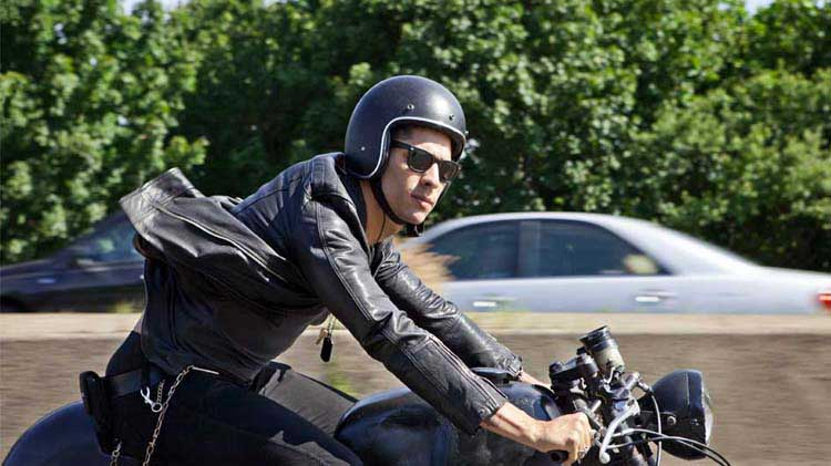 Wearing a helmet, a male motorcycle rider checks for oncoming traffic.