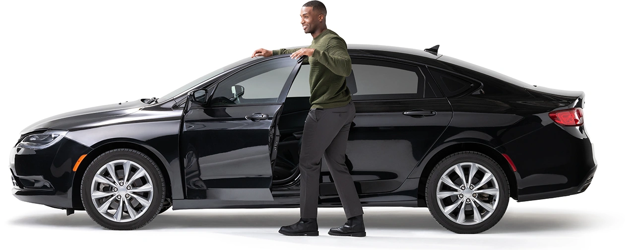 A young man stands by the open door of his midnight black car.