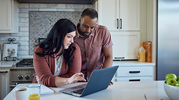 Standing in their kitchen, a couple check on their claim via their laptop.