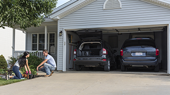 A couple plants flowers just outside their two-car garage. Combining their purchase of home and auto policies could save them money.