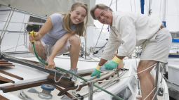 A smiling couple lean into the shot next to their sailboat.