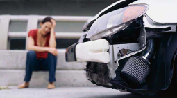 A woman sits on the curb staring at her damaged car.