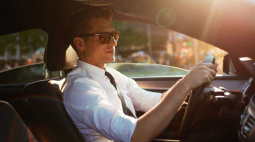 A man in a white shirt and blue tie grips the steering wheel.