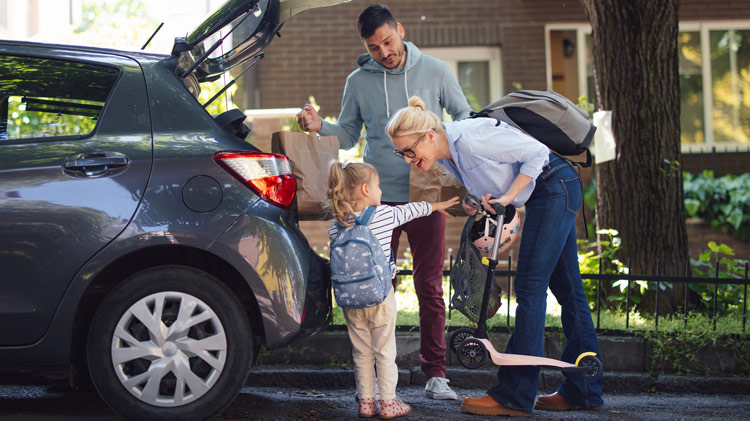 A family of three unpacks groceries from the back of their SUV.