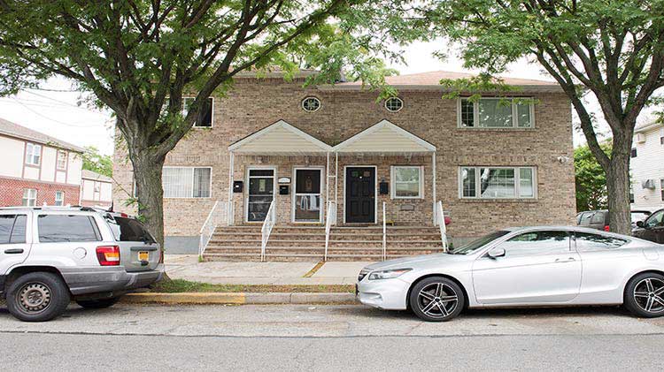 A white car is parked on the street in front of an apartment entrance.