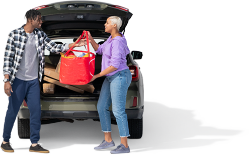 A woman in a periwinkle pullover hands a red bag of groceries to her spouse.