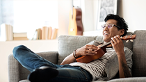 Content with his condo discount, a man reclines in his chair while strumming a ukulele.