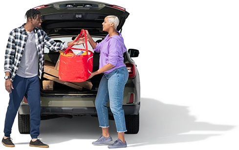 A woman in a periwinkle pullover hands a red bag of groceries to her spouse.