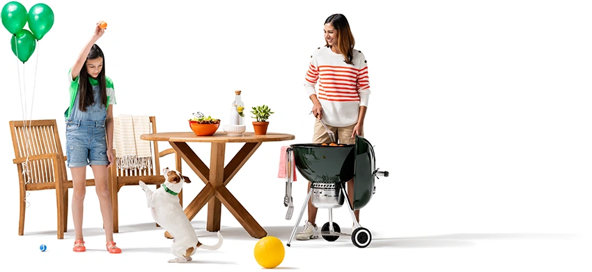 A woman grills as her daughter plays with their dog. Green balloons are tied to the patio chair.