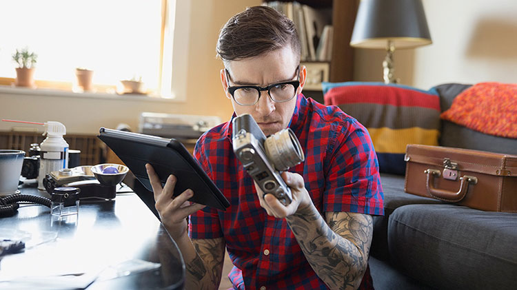 A man with glasses and a checkered flannel shirt inspects his camera.