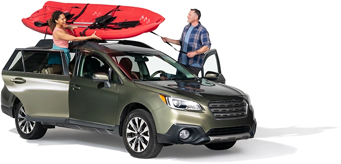 A couple secure a red raft atop their SUV