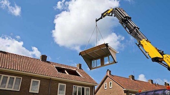 A crane moves a section of house into place