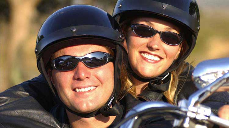 A helmeted woman smiles as she holds tight to her helmeted driver.