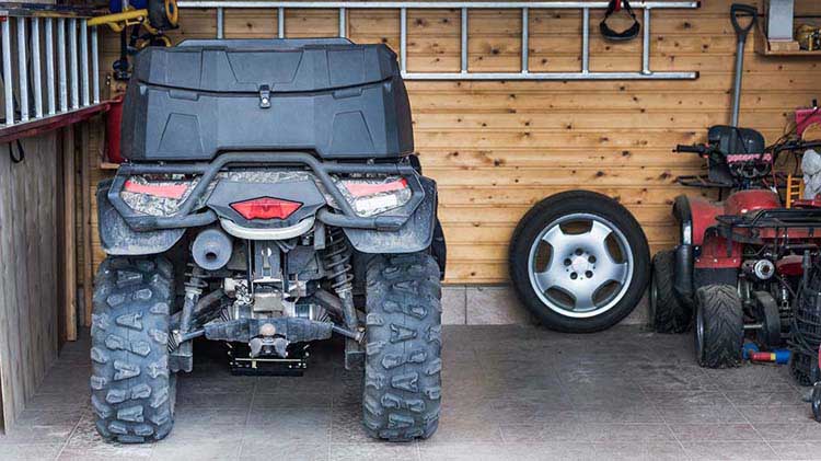 An ATV is parked in a garage next to a tire.