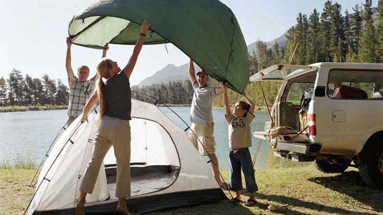 A family sets up a tent next to a lake.