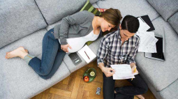 A couple review a list of items while relaxing on their grey couch.