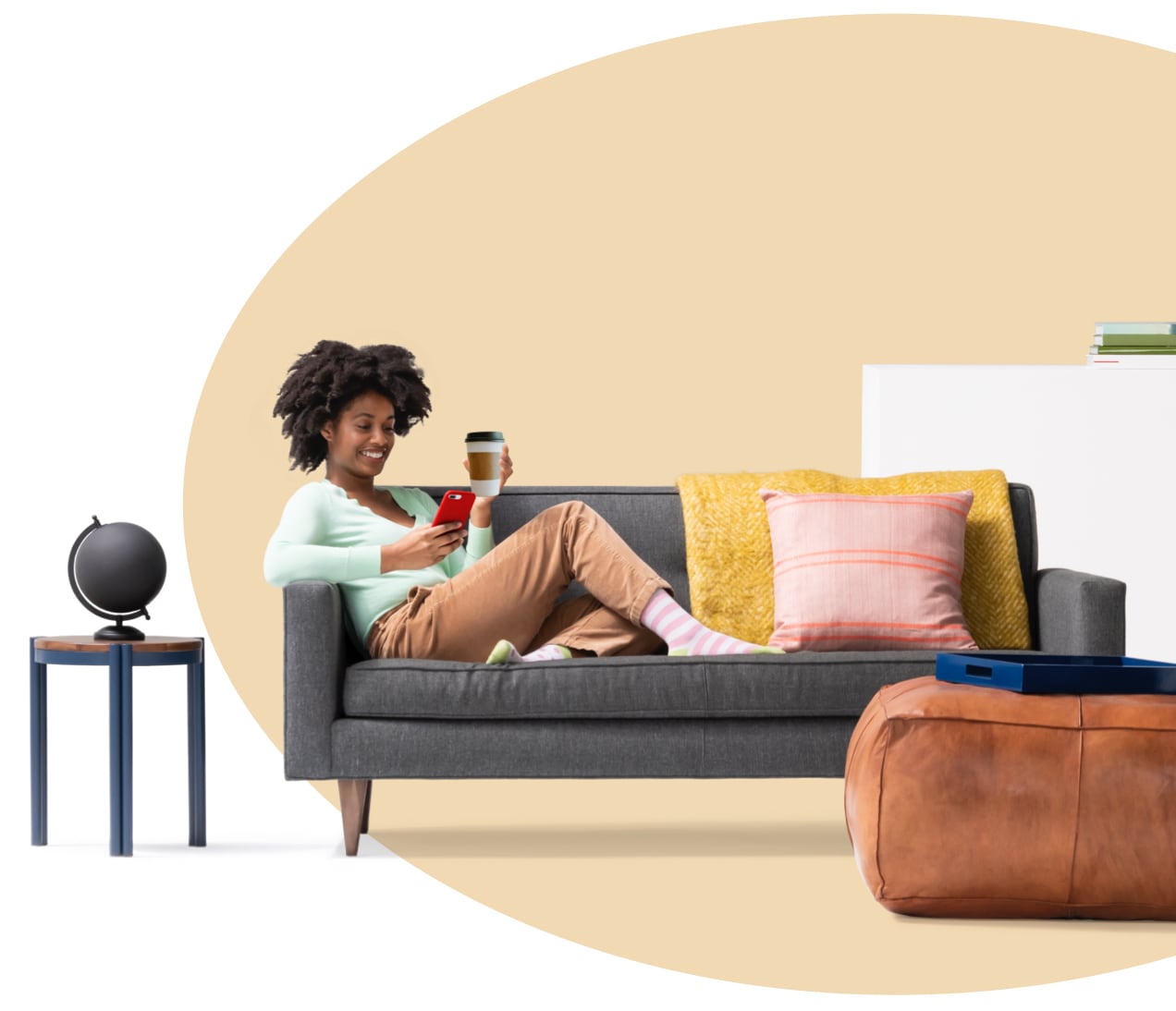 Woman sitting on couch holding a coffee while reading her iPhone about what renters insurance covers. A globe sits on side table.