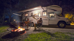 A family sits around a campfire outside their RV.