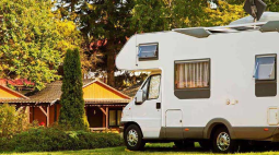 A motorhome parked outside a brick house with a tree in the front yard.