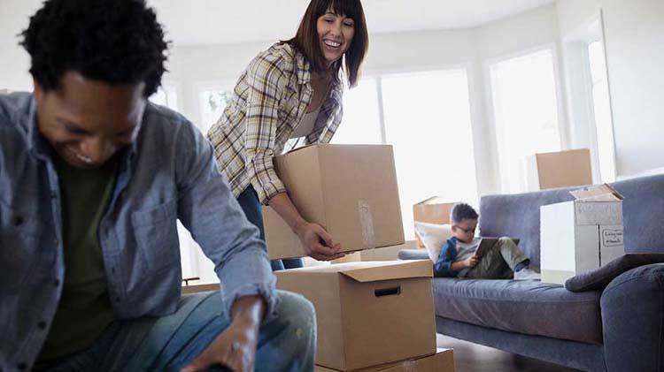 A couple unpack while their son reads on the couch.