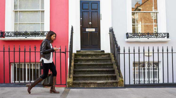 A woman approaches the stairs of a pink apartment building.