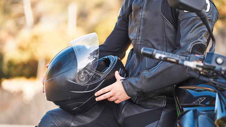 Un hombre con una chaqueta negra de cuero inspecciona un casco con visera.